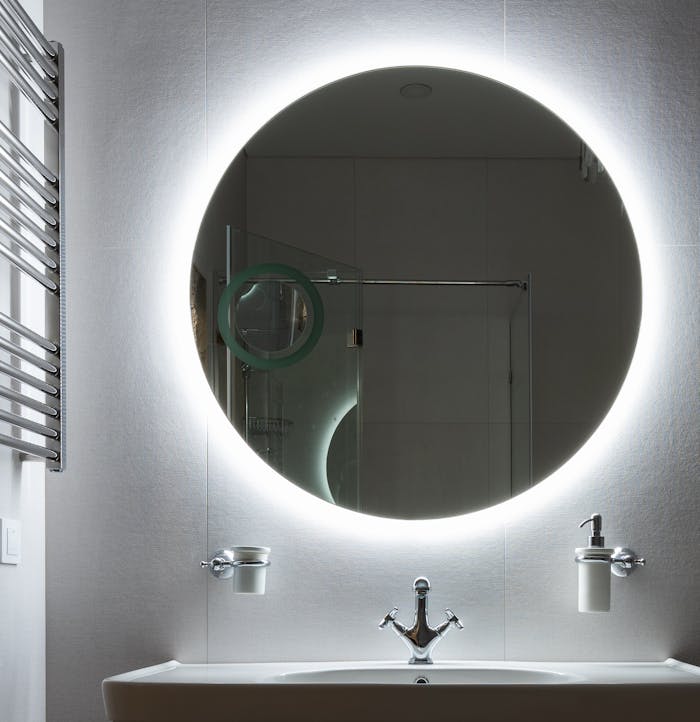 Contemporary bathroom with round shaped mirror above washstand and dispenser bottle in holder at home